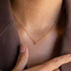 Model wearing a dainty gold bubble letter K charm necklace.