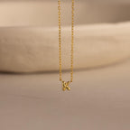 Close-up of the gold Custom Bubble Initial Necklace with the letter K, displayed on a neutral surface.