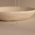Silver dainty bubble initial M charm necklace against a neutral background.