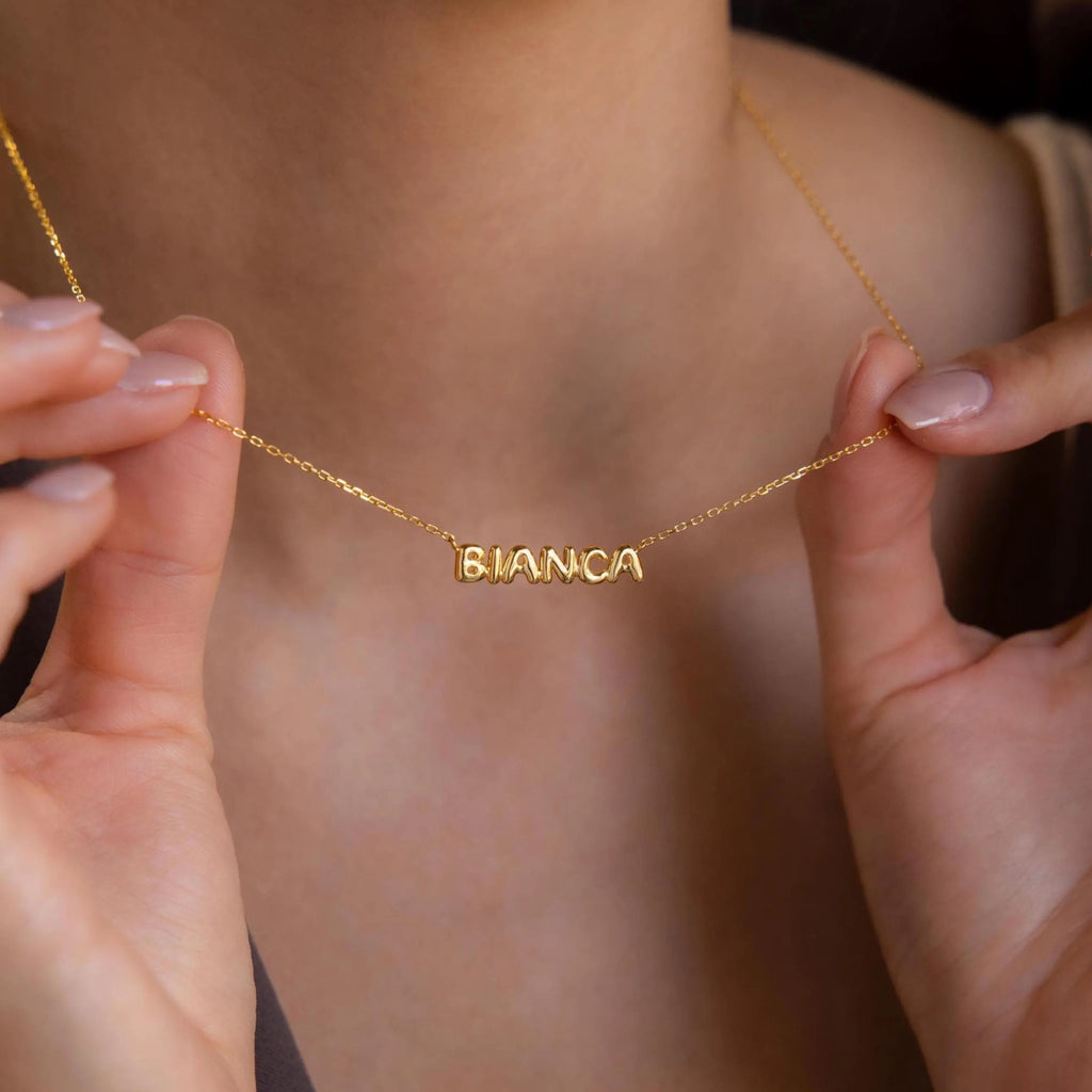 Model showcases a gold bubble name plate necklace of the name Bianca.