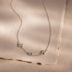 The Multiple Bubble Letter Necklace features M, O, and M bubble letter charms on a silver chain, displayed on beige textured paper—a unique boho accessory perfect for celebrating moms.