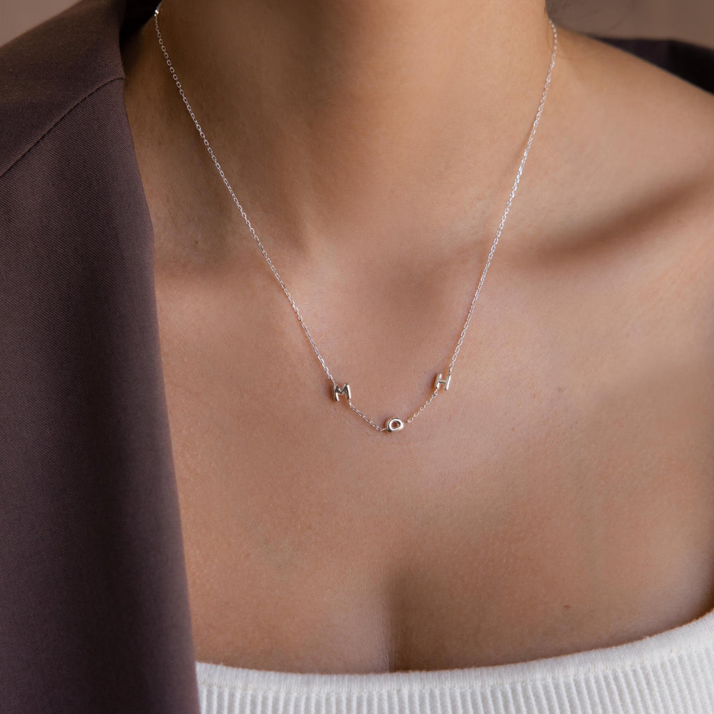 Model wears silver bubble letter necklace spelling “MDH”.