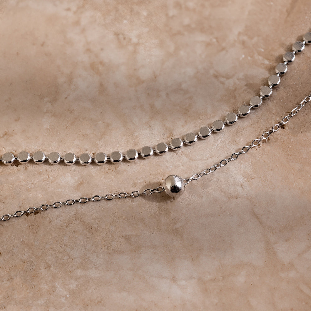 Silver beaded chain necklace on a beige stone surface