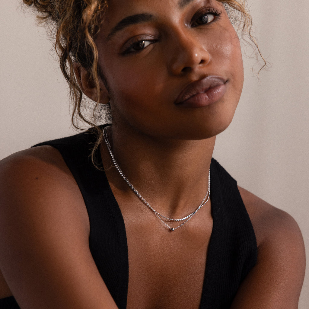 Woman wearing a black sleeveless top and silver layered beaded necklace against a neutral background