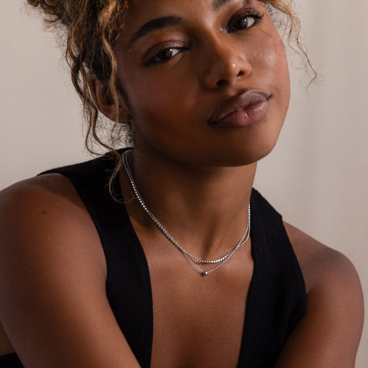 Woman wearing a black sleeveless top and silver layered beaded necklace against a neutral background