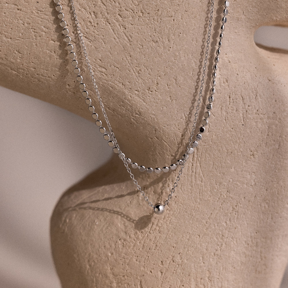 Silver beaded double chain necklace on a beige stone background
