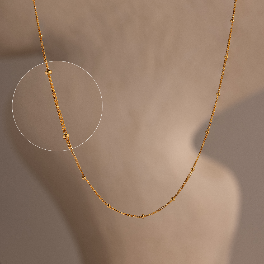 Gold beaded chain necklace on a neutral background