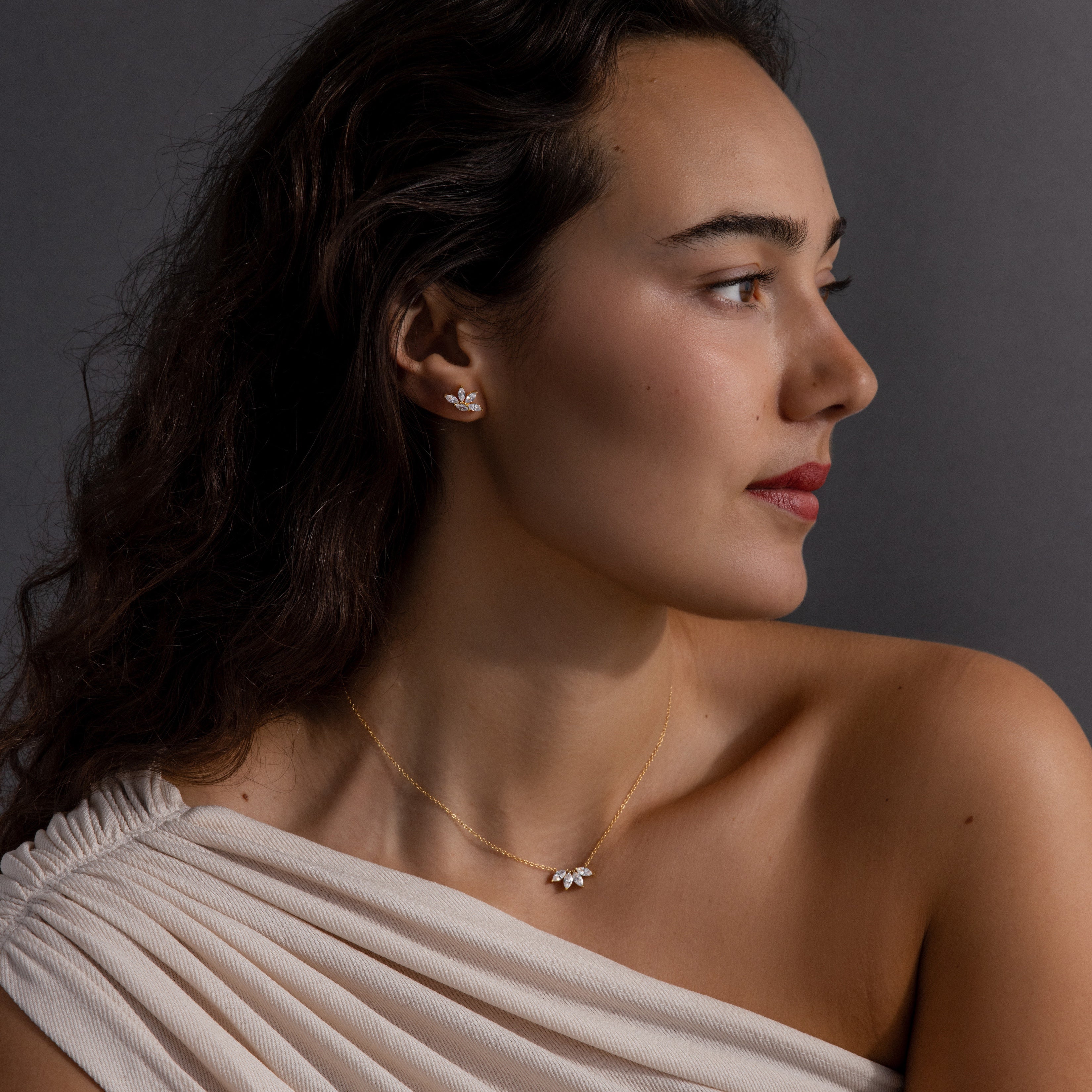A woman with long dark hair in an off-shoulder white top showcases the Marquise Diamond Jewelry Set, featuring a diamond necklace and matching earrings—an elegant choice for wedding jewelry.