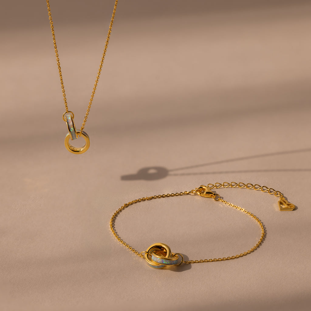 The Interlocking Opal Inlay Necklace and Bracelet Set in 18K Gold, featuring elegant circle pendants, rests on a beige surface with soft shadows for a refined look.
