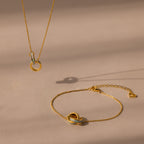 The Interlocking Opal Inlay Necklace and Bracelet Set in 18K Gold, featuring elegant circle pendants, rests on a beige surface with soft shadows for a refined look.