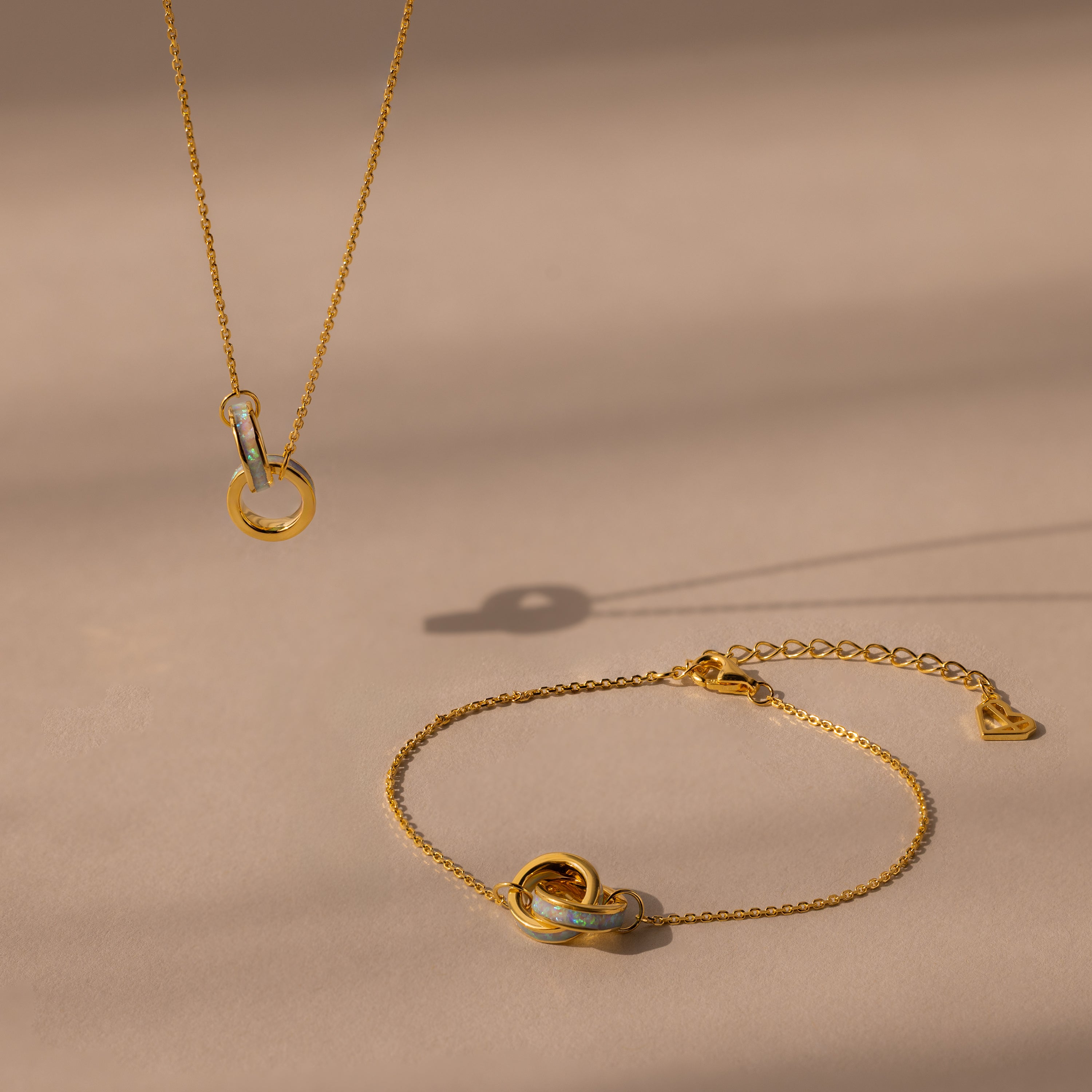 The Interlocking Opal Inlay Necklace and Bracelet Set in 18K Gold, featuring elegant circle pendants, rests on a beige surface with soft shadows for a refined look.