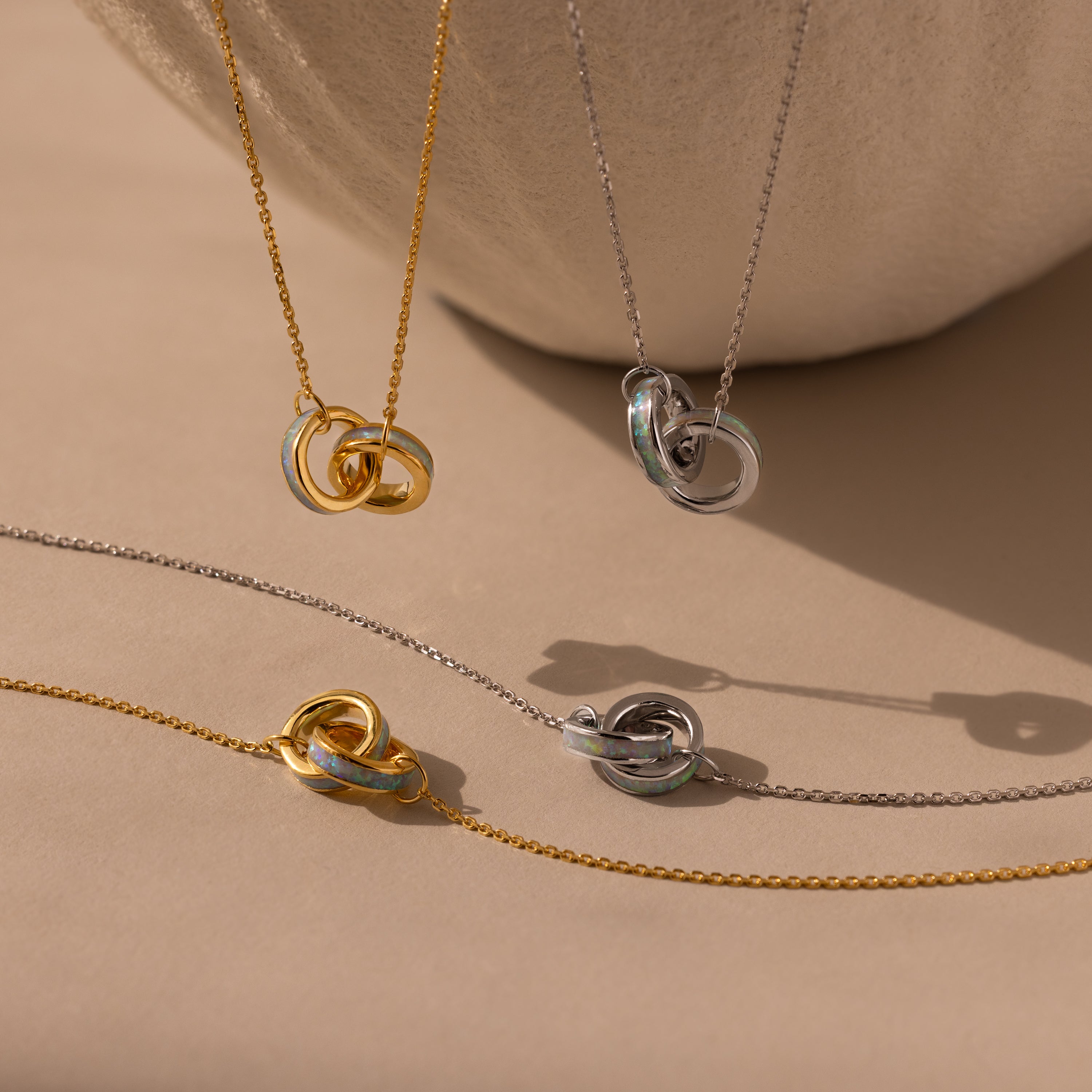 Two gold and two silver Interlocking Opal Inlay Necklace and Bracelet Sets are displayed on a beige surface with a soft shadow in the background.