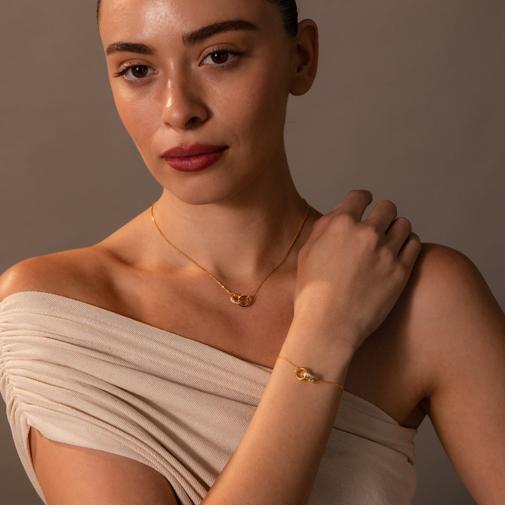 A woman models the Interlocking Opal Inlay Necklace and Bracelet Set, pairing it with an off-shoulder beige top against a plain background.