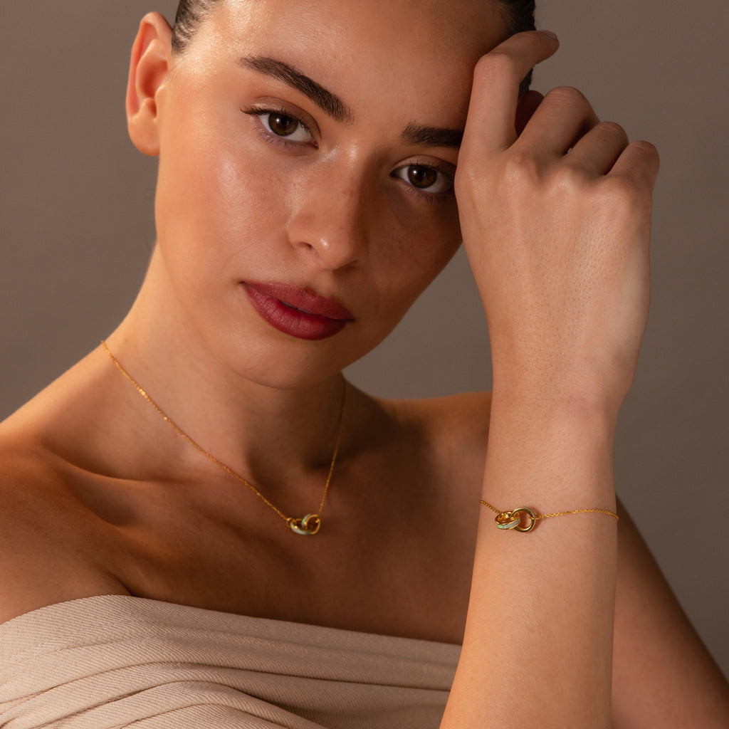 A woman poses with her hand near her face, wearing the Interlocking Opal Inlay Necklace and Bracelet Set in 18K Gold against a neutral background.