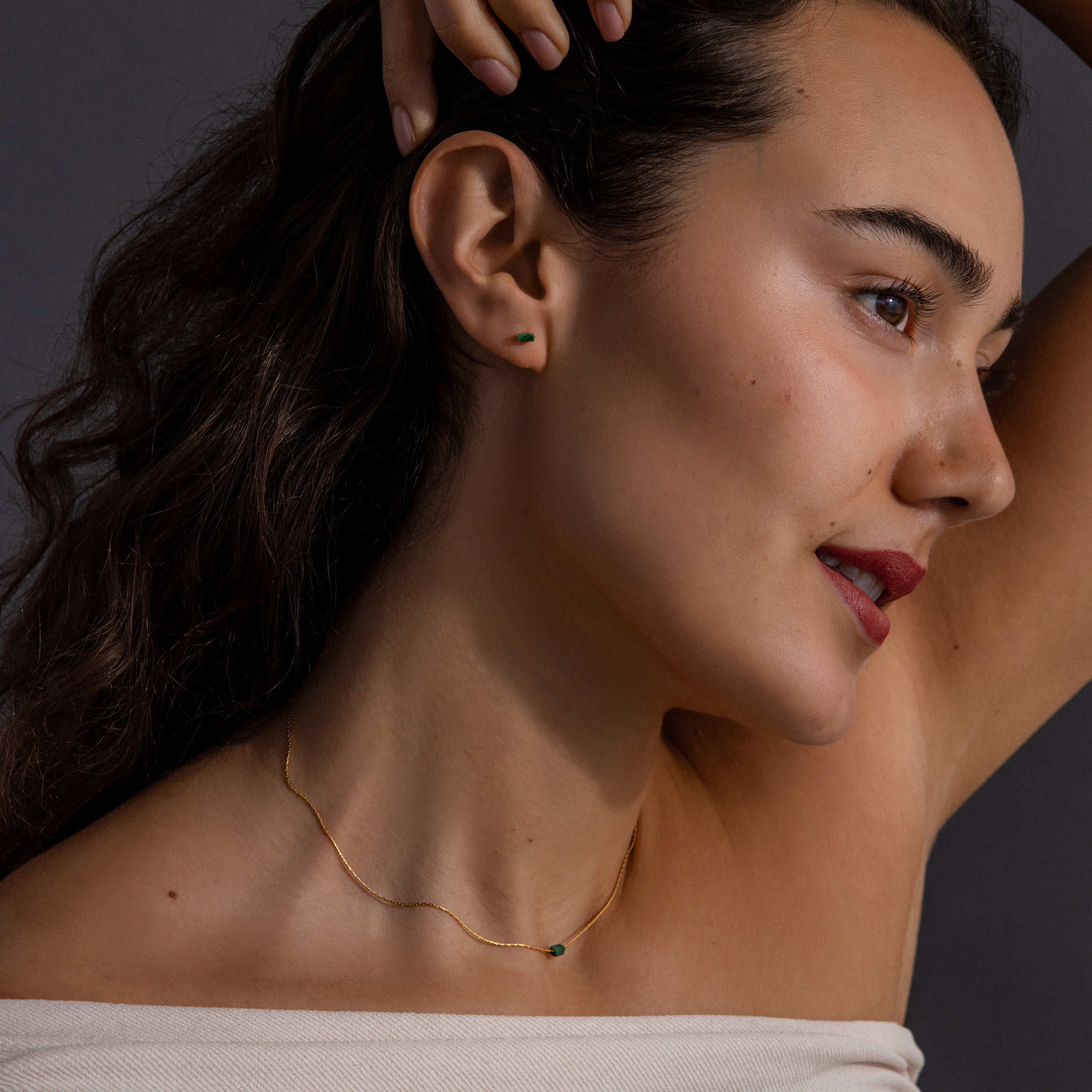 Woman with wavy brown hair poses in profile, wearing the Jade Bar Jewelry Set in 18K Gold, featuring a jade necklace and matching jade stud earrings.