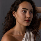 A woman with wavy brown hair, dressed in a white top and wearing the Jade Bar Jewelry Set, poses against a dark gray background.