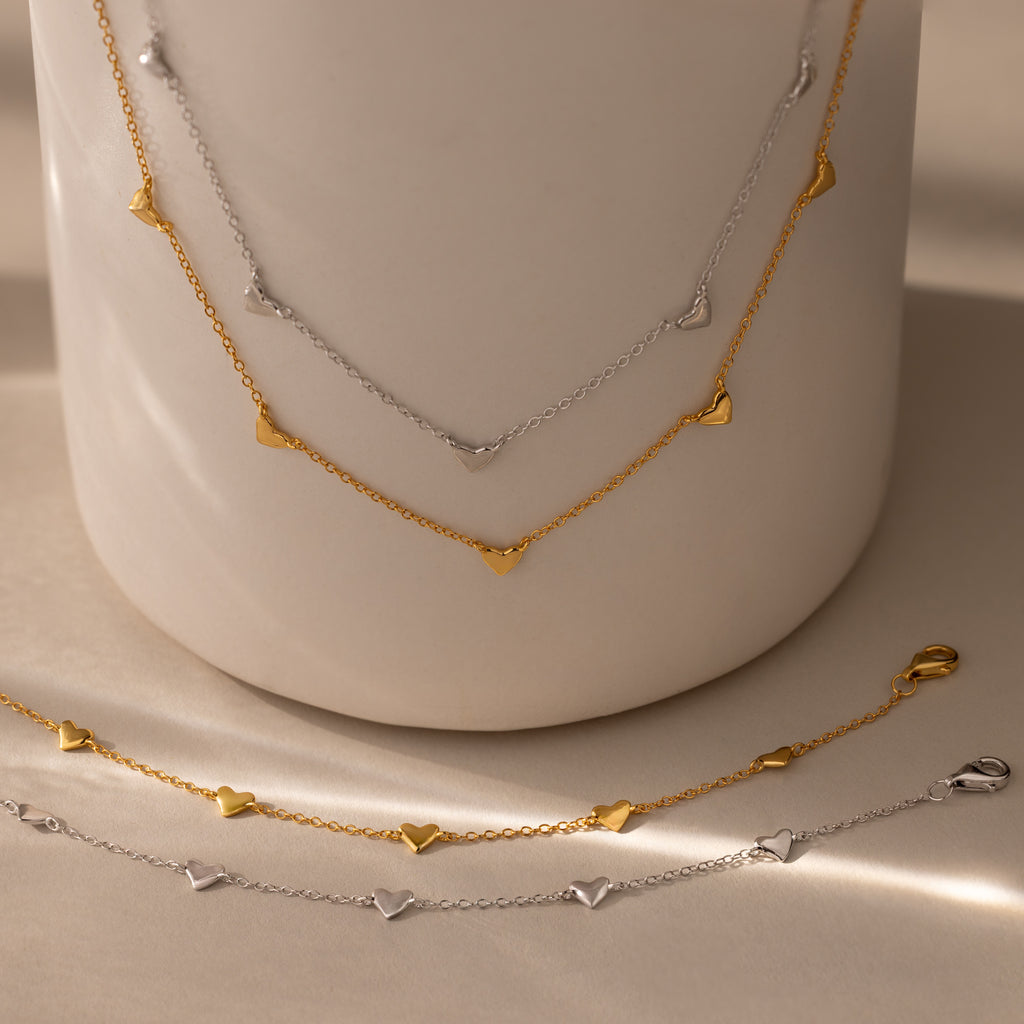 Heart Station Necklace & Bracelet Set, crafted in 18K gold and silver, displayed on a smooth, neutral surface.
