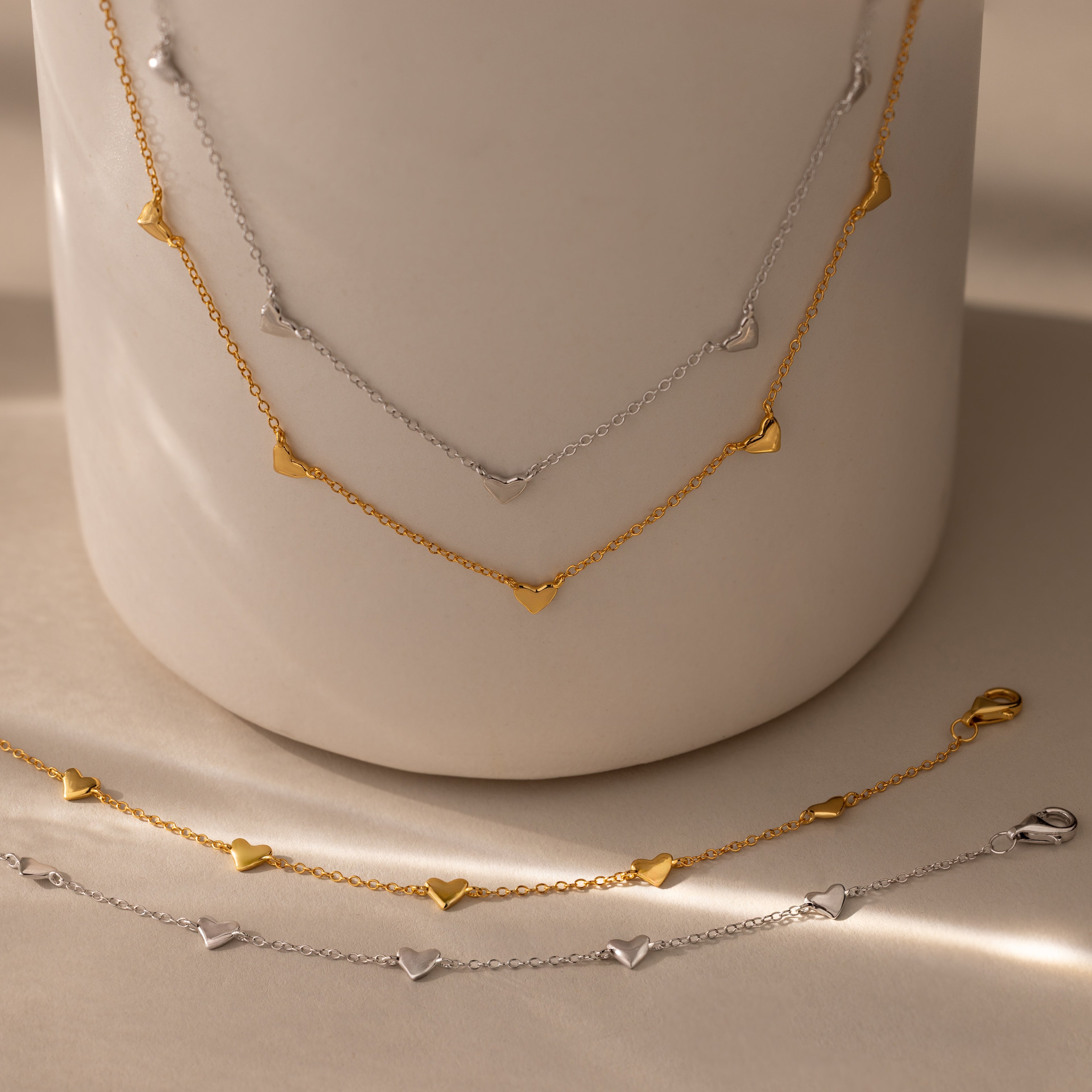 Heart Station Necklace & Bracelet Set, crafted in 18K gold and silver, displayed on a smooth, neutral surface.