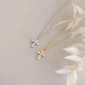 Two Pearl Cross Necklaces display pearl cross charms on gold and silver chains, shown on a light surface with dried leaves.