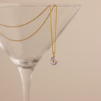 Gold North Star Birthstone Necklace with a Light Purple Alexandrite Gemstone hanging inside a cocktail glass.