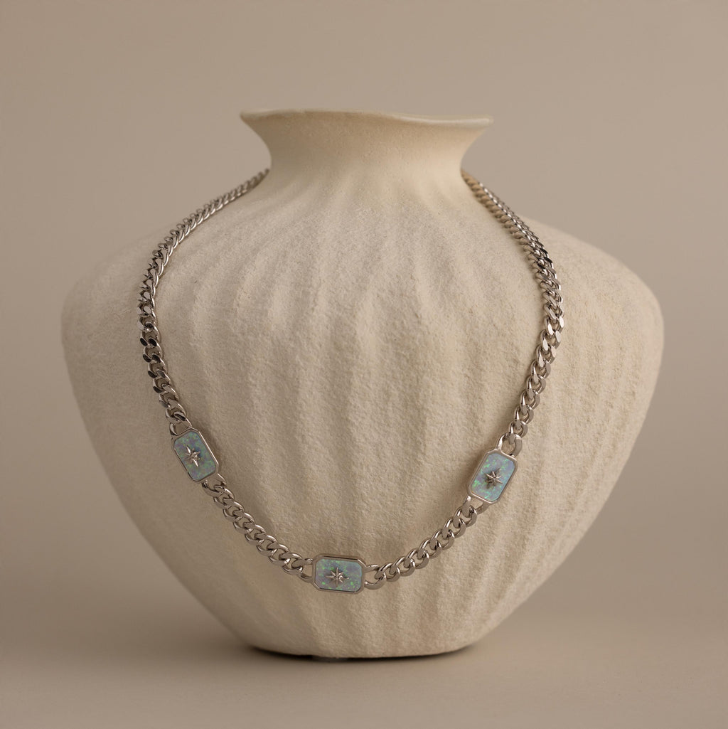 Silver North Star Opal Necklace displayed on a textured cream vase.
