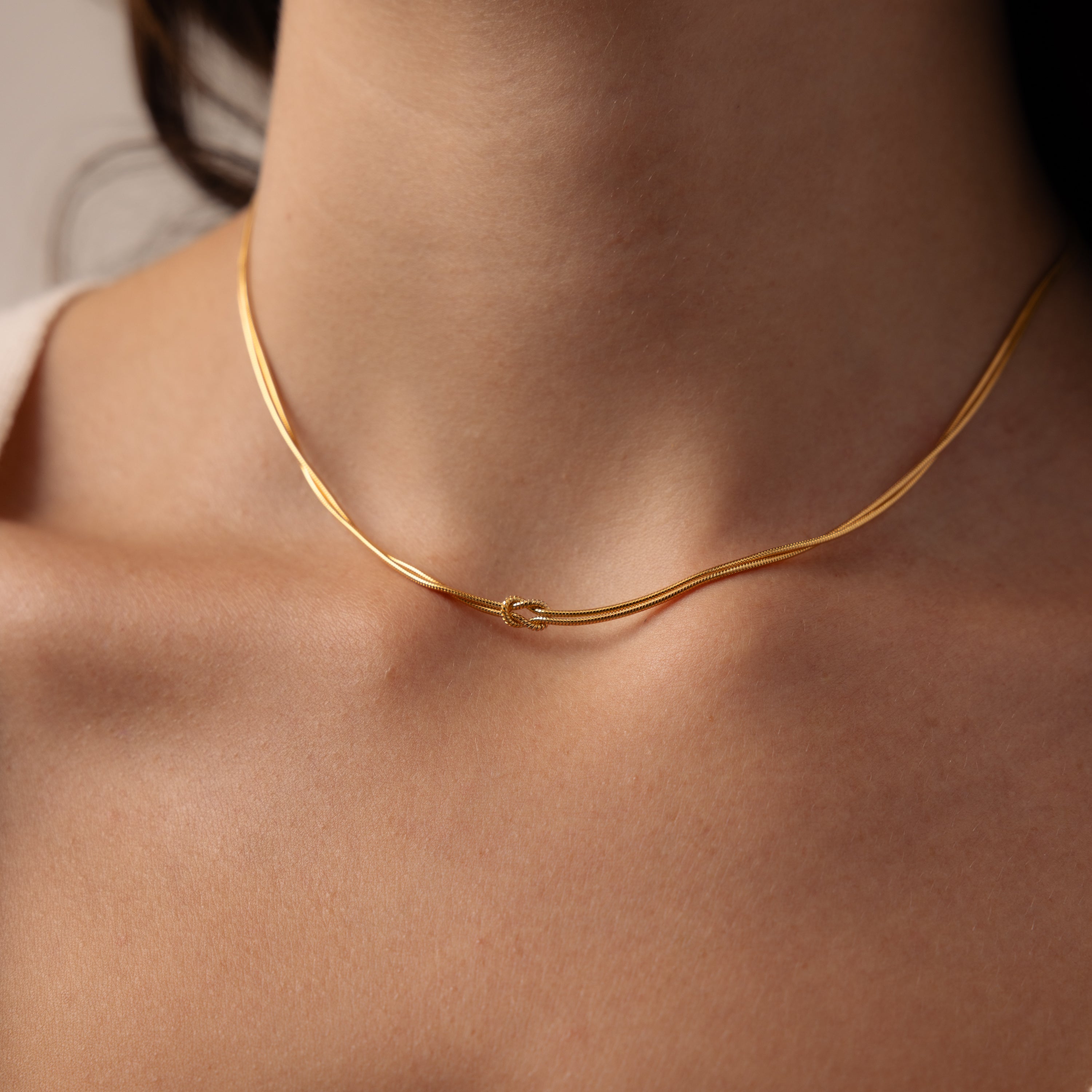 A close-up of a woman's neck wearing the Love Knot Chain Necklace, featuring a small knot detail at the center on a delicate gold snake chain.