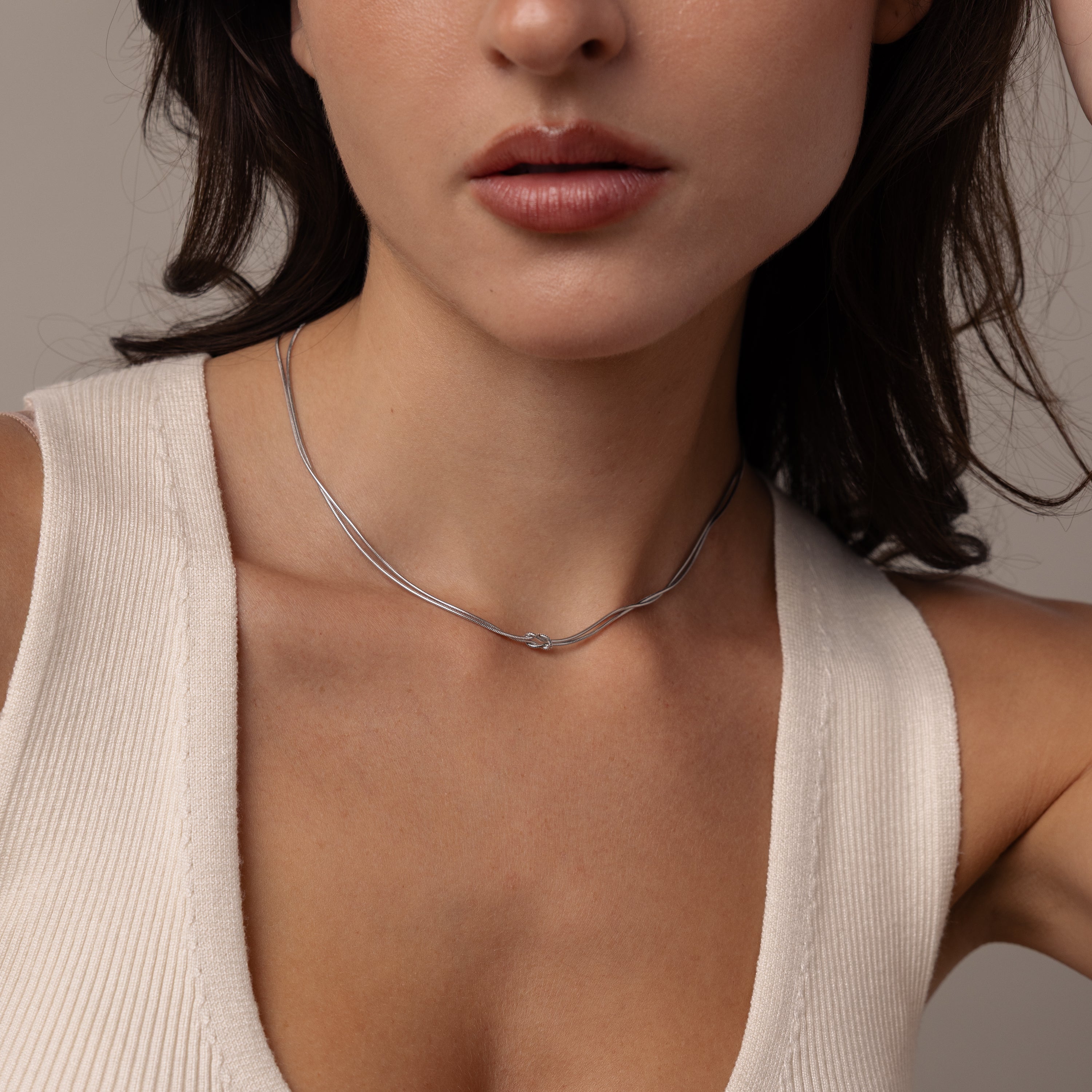 Woman wearing a cream sleeveless top and the Love Knot Chain Necklace, shown from shoulders to lips.