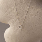 The Large Rolo Clasp Necklace in Sterling Silver features a delicate circle pendant, displayed on a textured beige mannequin—a versatile piece for effortless elegance.