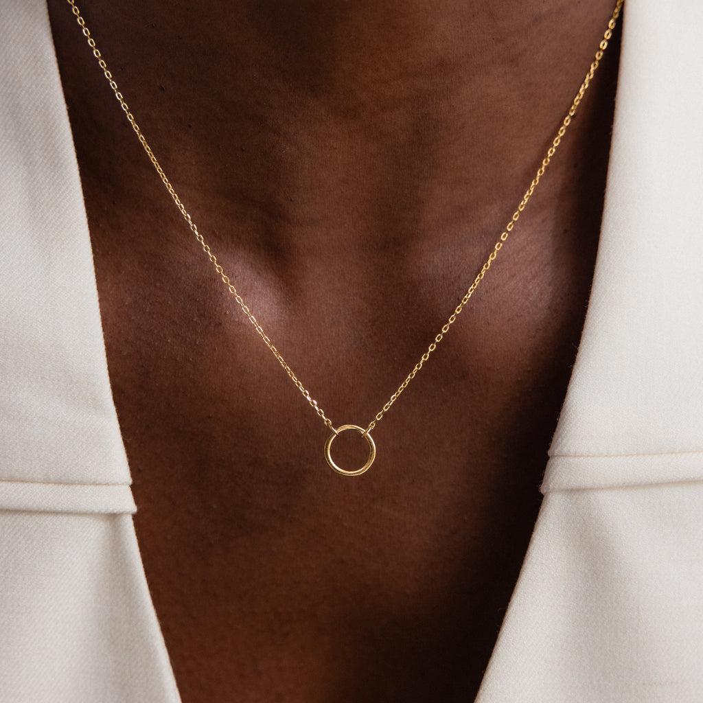 The Large Rolo Clasp Necklace, a bold gold chain with a circular pendant, is styled over a white blazer to bring a modern essential touch to any outfit.