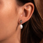 A close-up of a woman’s ear wearing the Midnight Pearl Drop Earrings in Sterling Silver—timeless jewelry featuring a small round stone and subtle black accents.