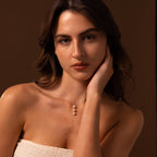 A woman with long brown hair rests her head on her hand, wearing a strapless top and the Pearl Cascade Necklace in Sterling Silver, an elegant accessory featuring luminous pearls.