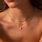 Close-up of a woman wearing layered gold necklaces, featuring the Pearl Dot Necklace with a delicate single pearl pendant, against bare skin.