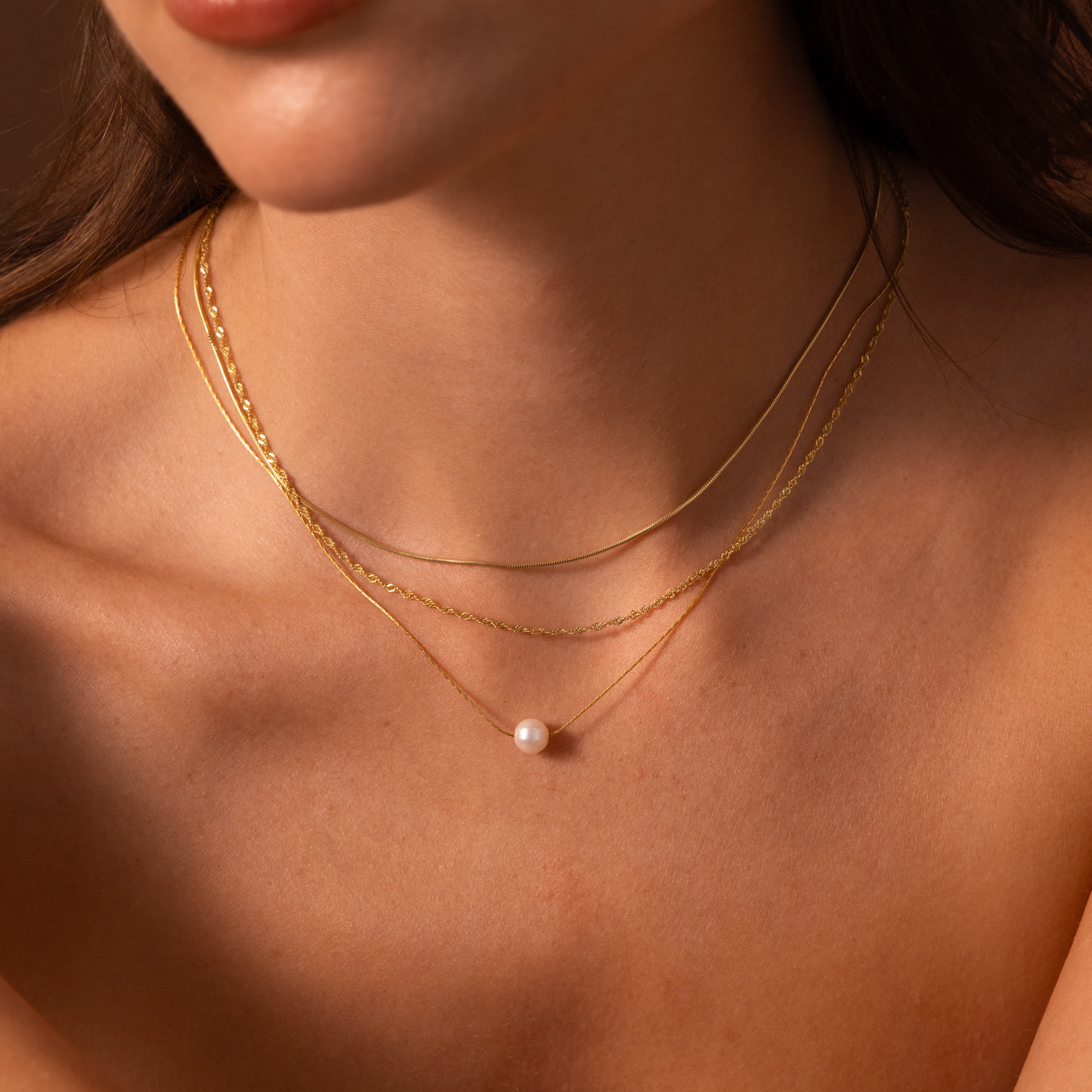 Close-up of a woman wearing layered gold necklaces, featuring the Pearl Dot Necklace with a delicate single pearl pendant, against bare skin.