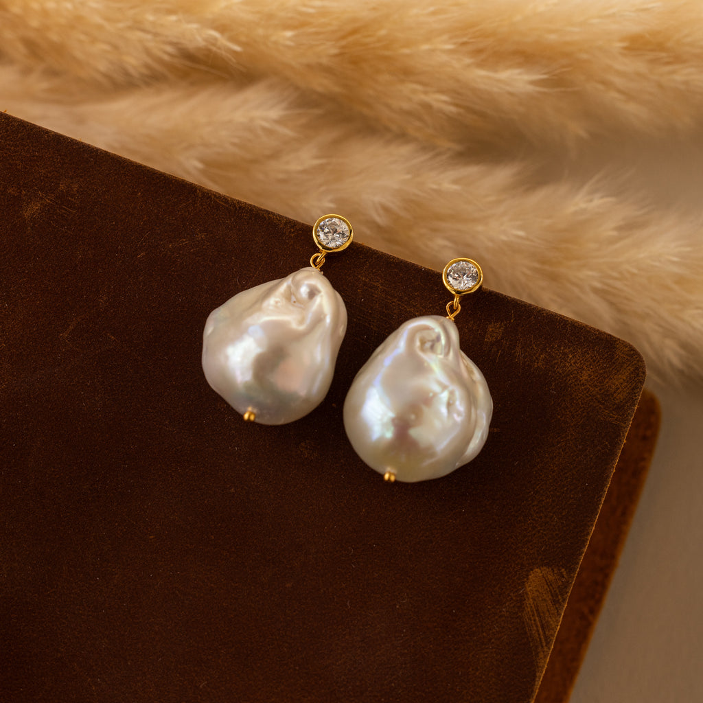 Diamond Baroque Pearl Studs in 18K Gold feature large baroque pearls and small diamonds, shown on brown velvet—a timeless piece of organic pearl jewelry.