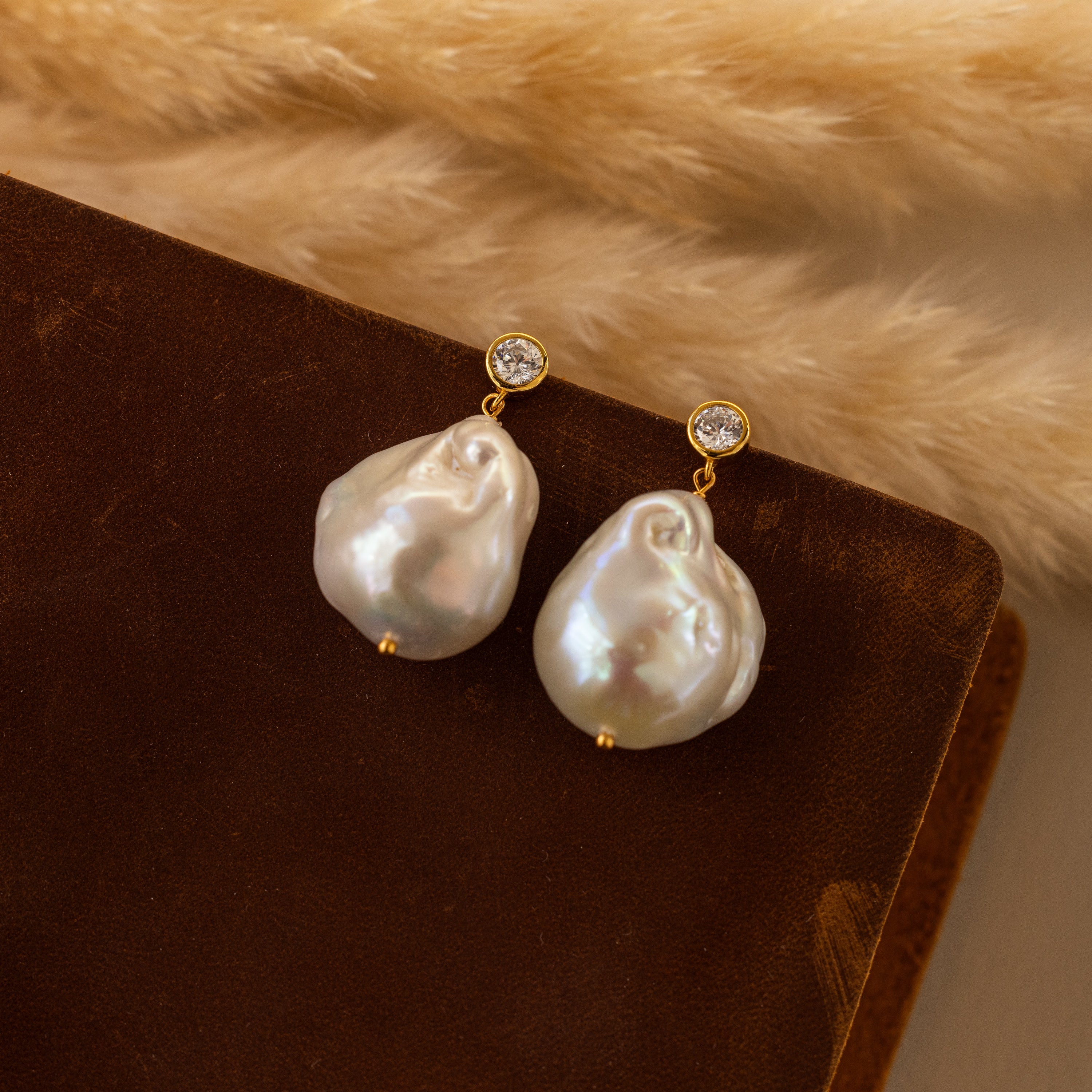 Diamond Baroque Pearl Studs in 18K Gold feature large baroque pearls and small diamonds, shown on brown velvet—a timeless piece of organic pearl jewelry.