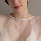 Woman wearing a sheer white top and the Pearl Cross Necklace in Silver, featuring a luminous pearl cross charm.