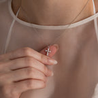 Someone holds the Pearl Cross Necklace in Silver, featuring luminous pearls and a small cross charm, set against a sheer white top.