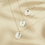 Three silver necklaces with oval pendants featuring engraved floral designs on a beige fabric background.