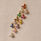 Butterfly Garnet Flatback Studs with colorful gemstones are arranged diagonally on a beige surface—perfect for anyone looking for unique flatback earrings or personalized jewelry.