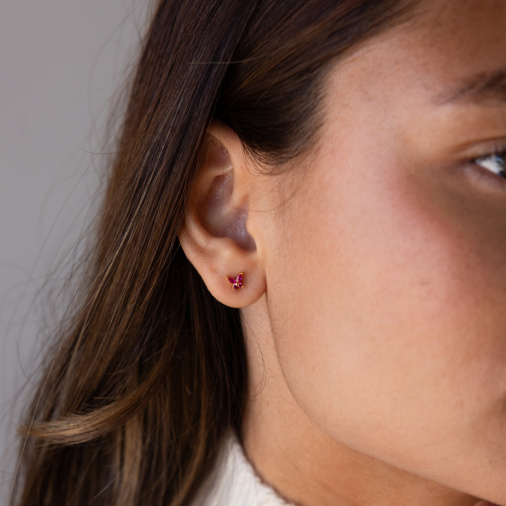 Close-up of a woman’s ear wearing Butterfly Ruby Flatback Studs, small red butterfly birthstone earrings perfect for personalized jewelry lovers.