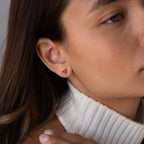 Close-up of a woman with long brown hair in a white turtleneck, wearing Butterfly Ruby Flatback Studs.