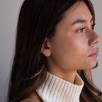 Woman with long brown hair in a cream turtleneck, wearing delicate Butterfly Diamond Flatback Studs and looking to the right.