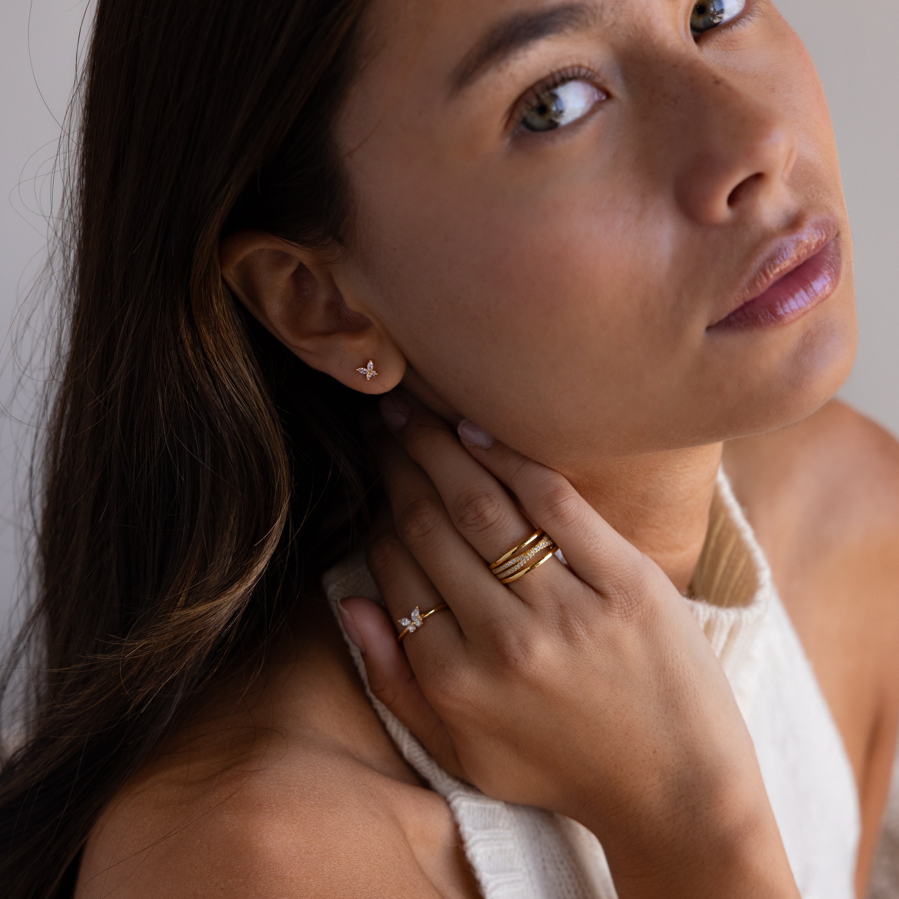 A woman with long brown hair wears gold rings and Butterfly Birthstone Flatback Studs, gazing up at the camera—a perfect showcase for personalized jewelry.