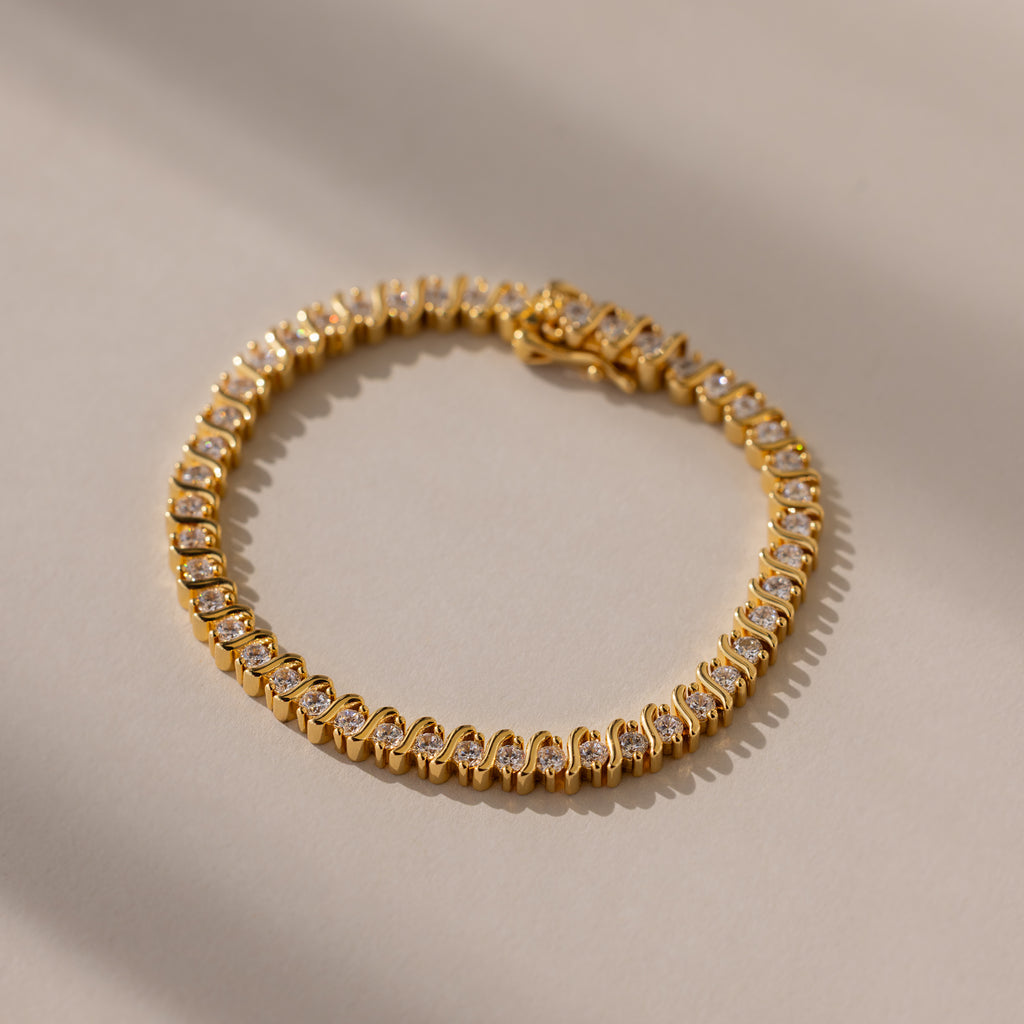 The S-Link Diamond Tennis Bracelet in 18K Gold, arranged in a circle on a sunlit, neutral surface, is an elegant jewelry piece with sparkling diamonds—perfect for any occasion.