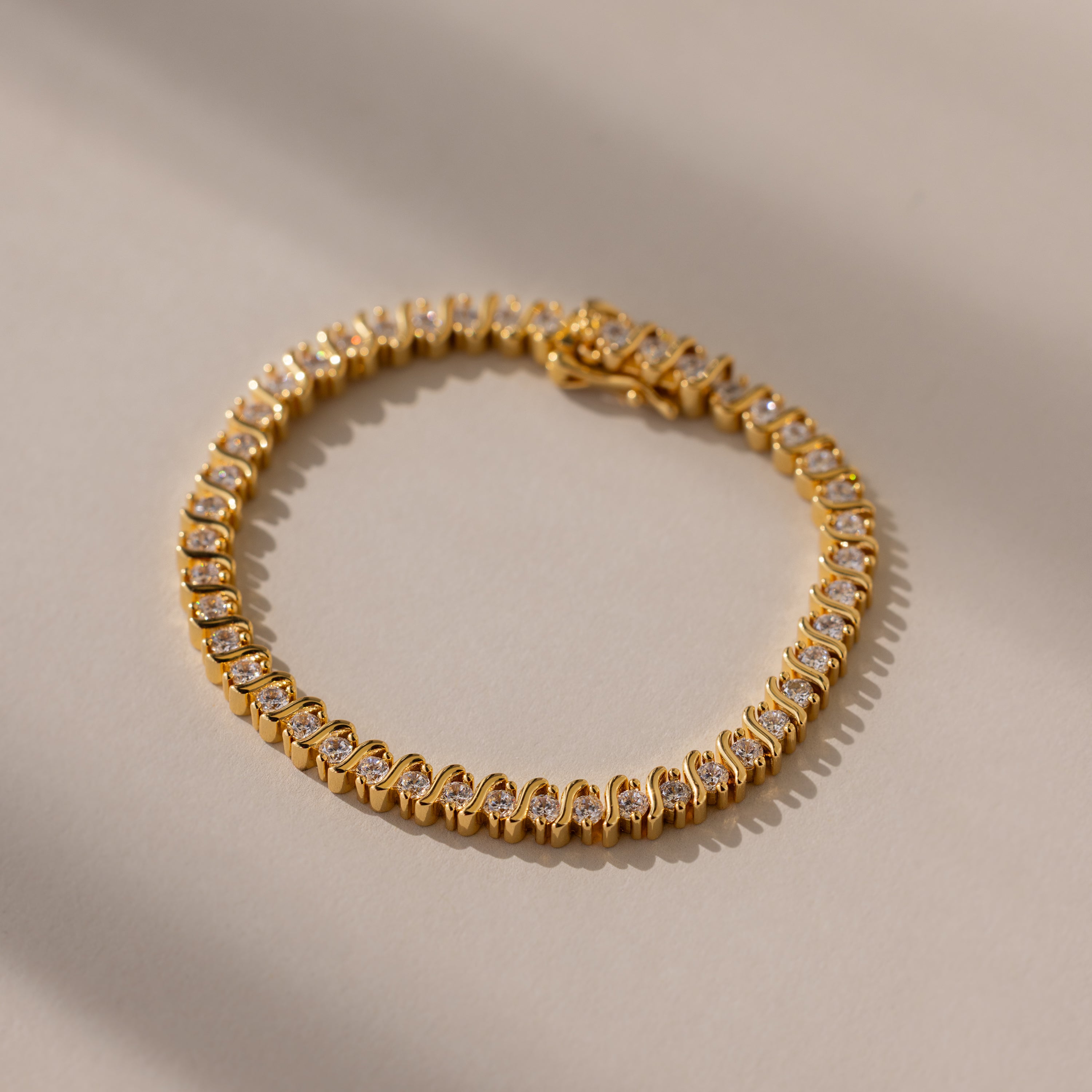 The S-Link Diamond Tennis Bracelet in 18K Gold, arranged in a circle on a sunlit, neutral surface, is an elegant jewelry piece with sparkling diamonds—perfect for any occasion.