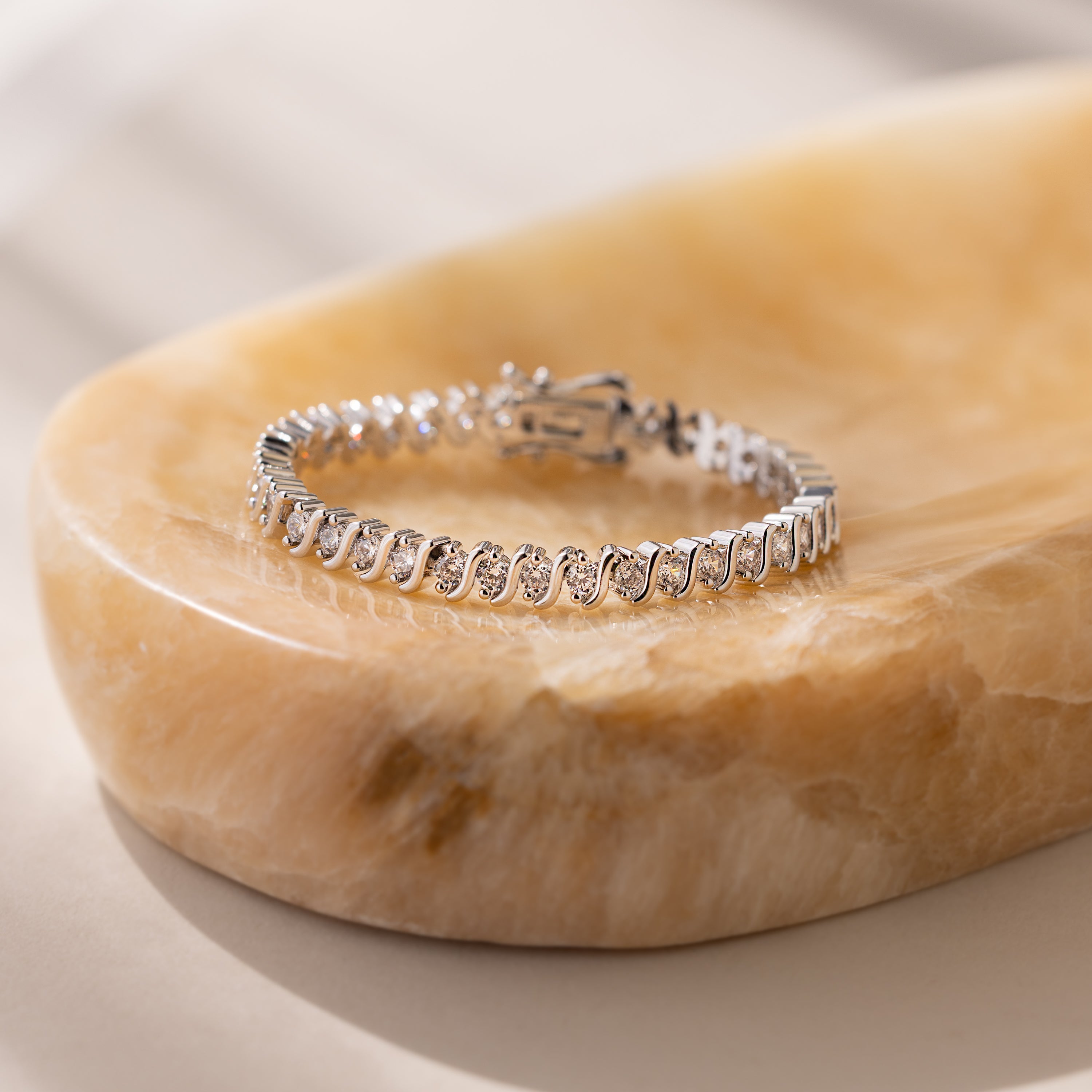 The S-Link Diamond Tennis Bracelet in White Gold features sparkling oval links, beautifully displayed on a smooth marble surface under soft lighting—a refined choice for jewelry lovers.