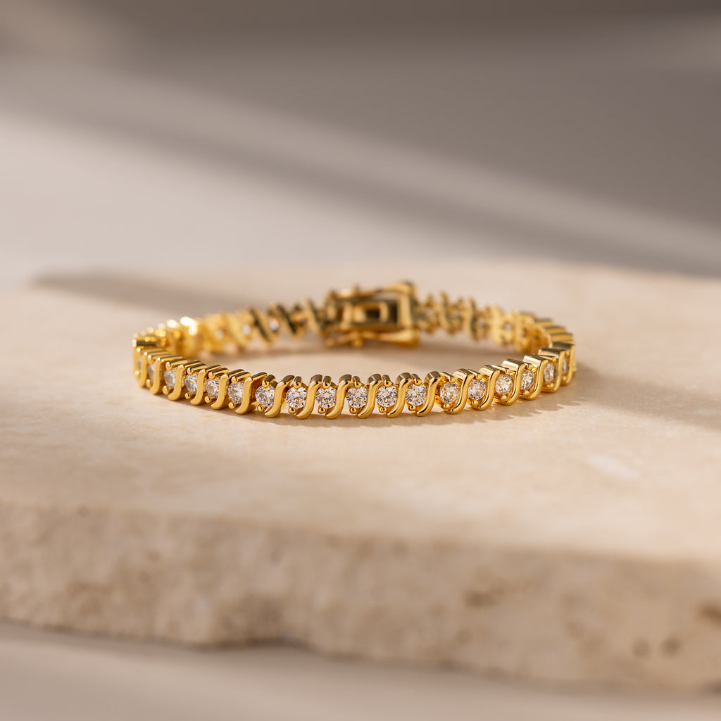 S-Link Diamond Tennis Bracelet in 18K Gold with diamond accents is elegantly displayed on a light stone surface with soft lighting.