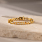 S-Link Diamond Tennis Bracelet in 18K Gold with diamond accents is elegantly displayed on a light stone surface with soft lighting.