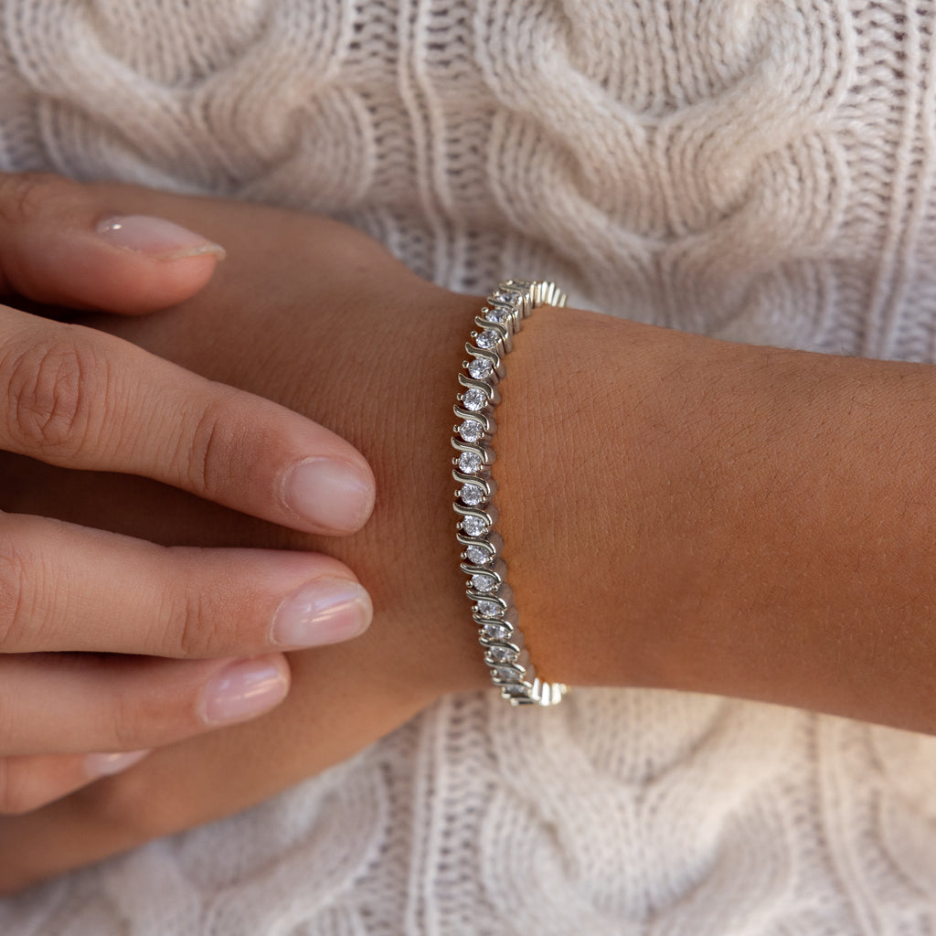 Close-up of a hand wearing the S-Link Diamond Tennis Bracelet in White Gold, showcasing sparkling diamonds against a cream knit sweater background.