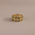 Gold checkered band ring featuring alternating rows of emerald and diamond round-cut CZ stones set in an openwork grid design, displayed on a neutral background.